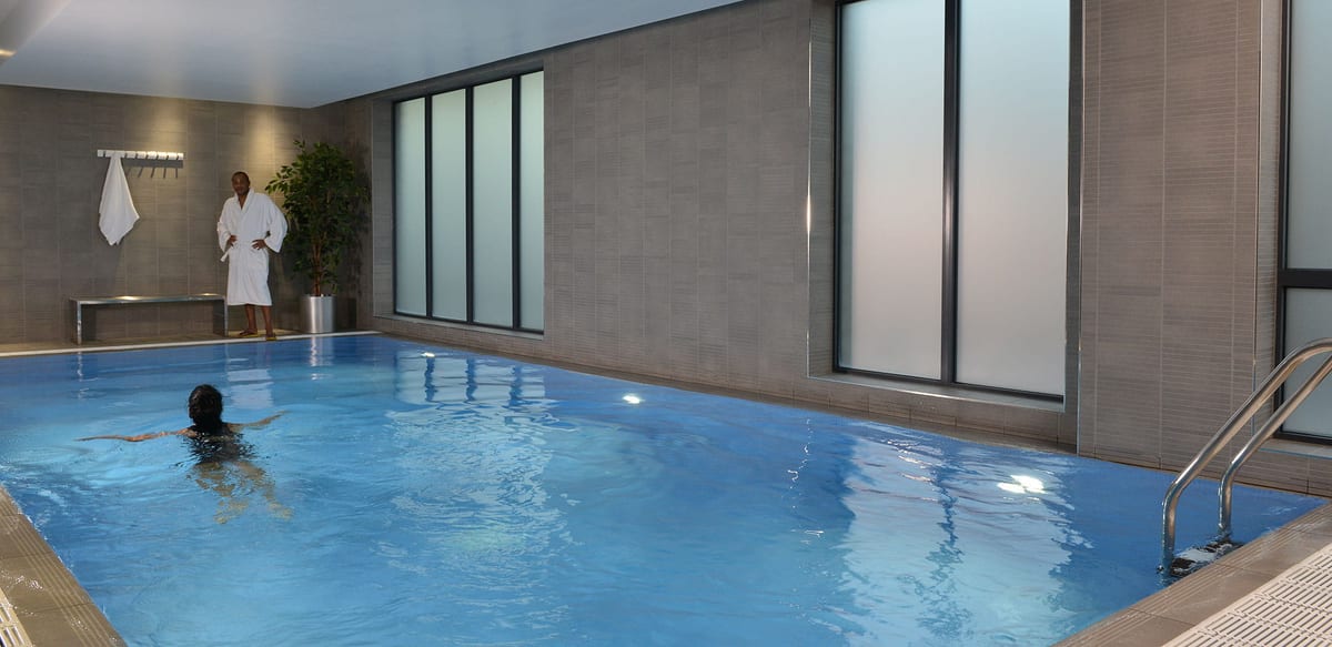 The Clubhouse swimming pool, with a swimmer in the water and a resident in a white robe beside frosted windows
