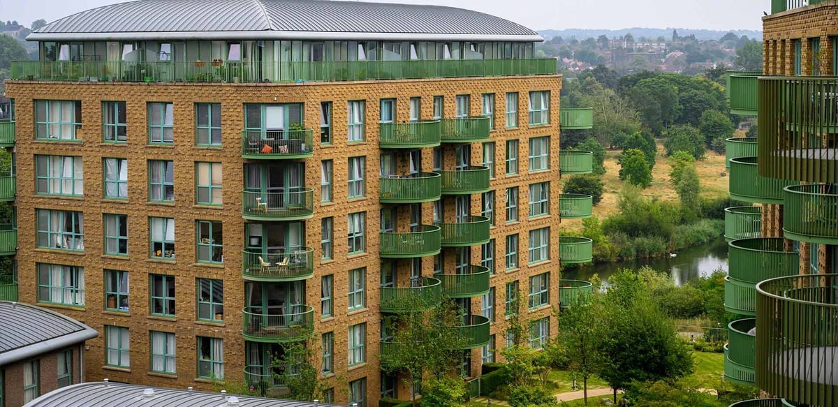 Waterlily Court's golden-brick building with green balconies, set against the trees and lake of South Cator Park