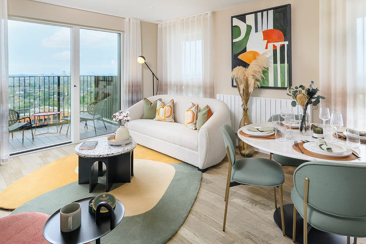 Show apartment living and dining room with a cream sofa, a round table with sage chairs and a balcony looking over treetops