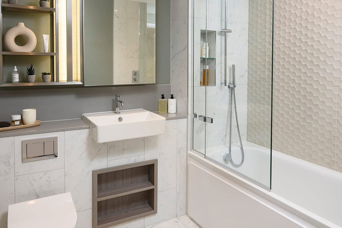Show apartment bathroom with textured white tiles, a mirrored cabinet, a white basin and a bath with a glass screen