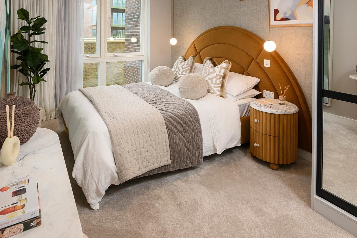 Show apartment bedroom with an arched ochre headboard, white bedding and a round bedside table